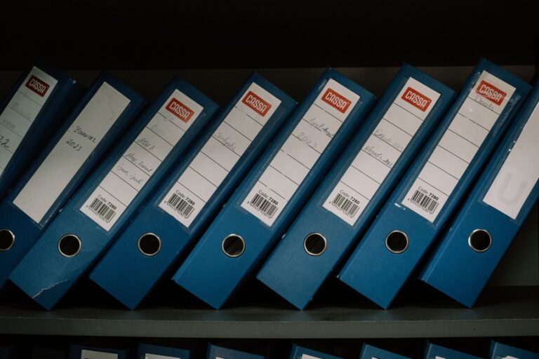 Classeurs de bureau bleus soigneusement disposés, étiquetés avec des dates et des noms pour un rangement organisé.