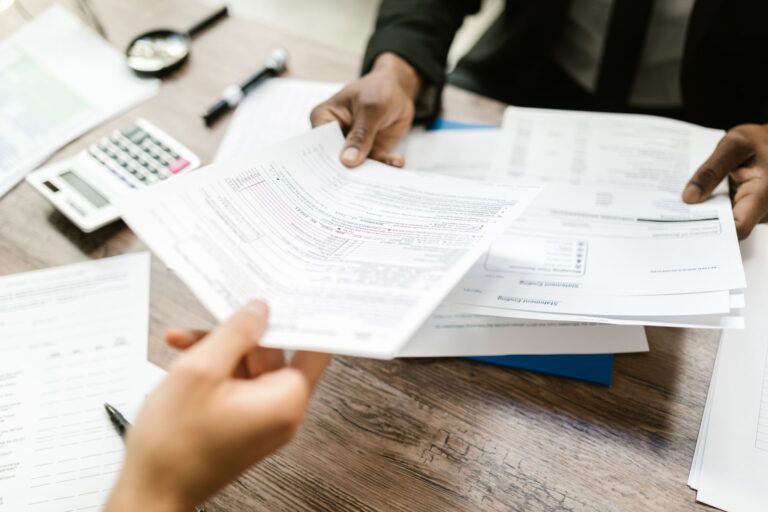 Deux professionnels échangeant des documents dans un bureau, se concentrant sur la paperasse et l'analyse des données.