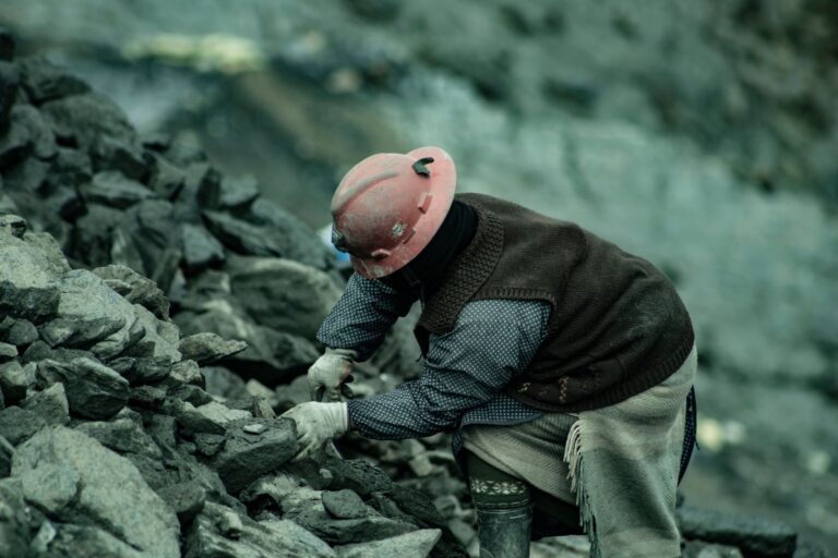 Un mineur de charbon portant un casque de sécurité travaillant dans un terrain rocheux, soulignant le travail et la résilience.