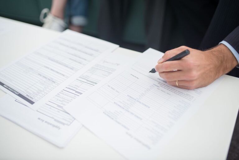 Gros plan d'une main signant des documents d'assurance dans un bureau.