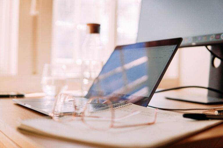 Un bureau à domicile bien éclairé avec un ordinateur portable, un écran et des lunettes, idéal pour le travail à distance.