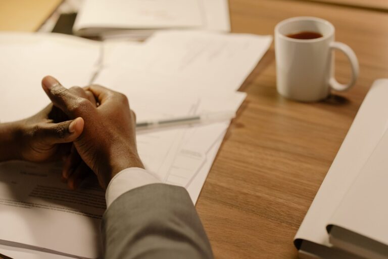 Gros plan des mains d'un professionnel à un bureau avec du café et des documents.
