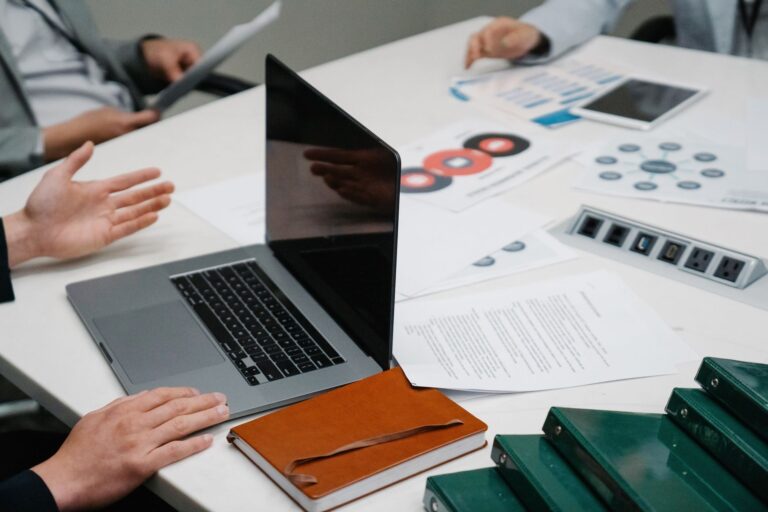 Gros plan d'une table de réunion avec un ordinateur portable, des documents et une discussion en cours.