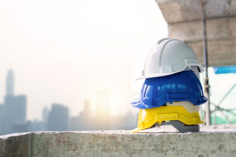 Trois casques de sécurité colorés empilés sur une surface en béton avec la ligne d'horizon de la ville en arrière-plan.