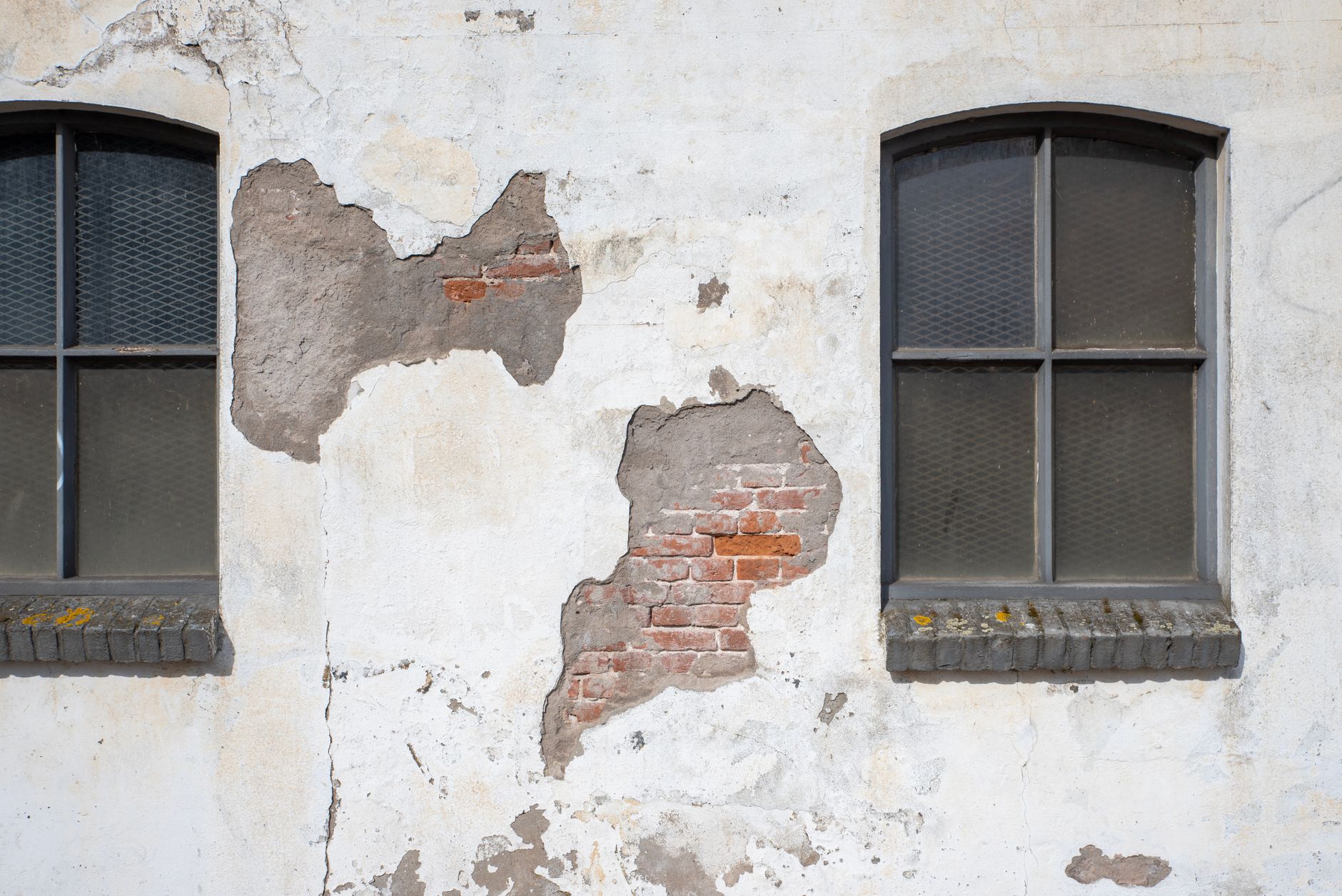 Façade ancienne dont l’enduit fissuré s’est détaché, laissant voir la brique entre deux fenêtres