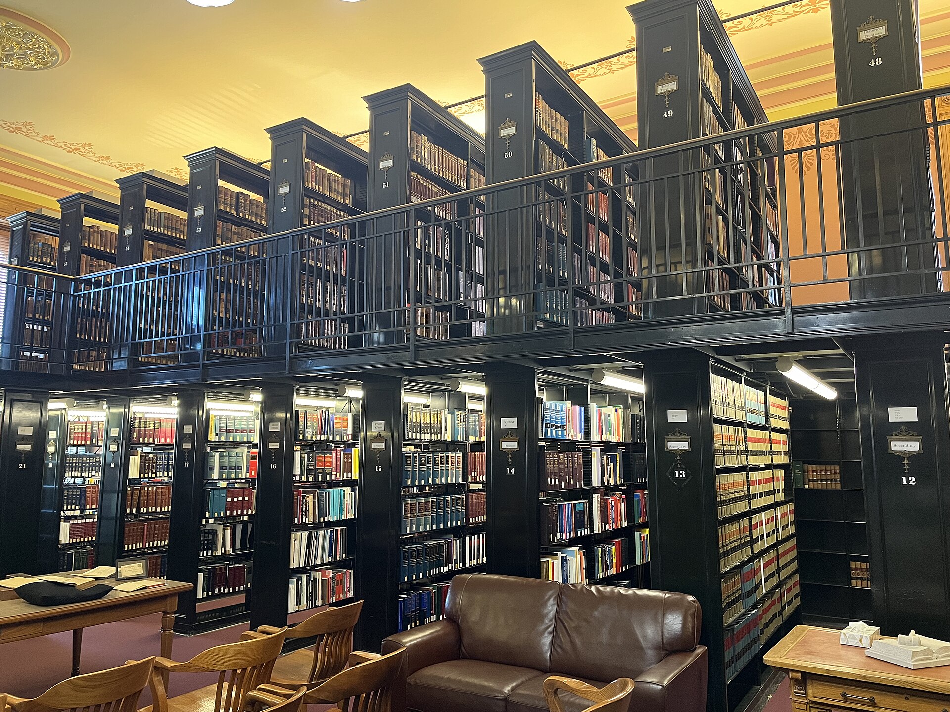 Bibliothèque juridique sur deux niveaux, avec rayonnages en bois sombre chargés d'ouvrages reliés, tables de lecture et canapé en cuir.