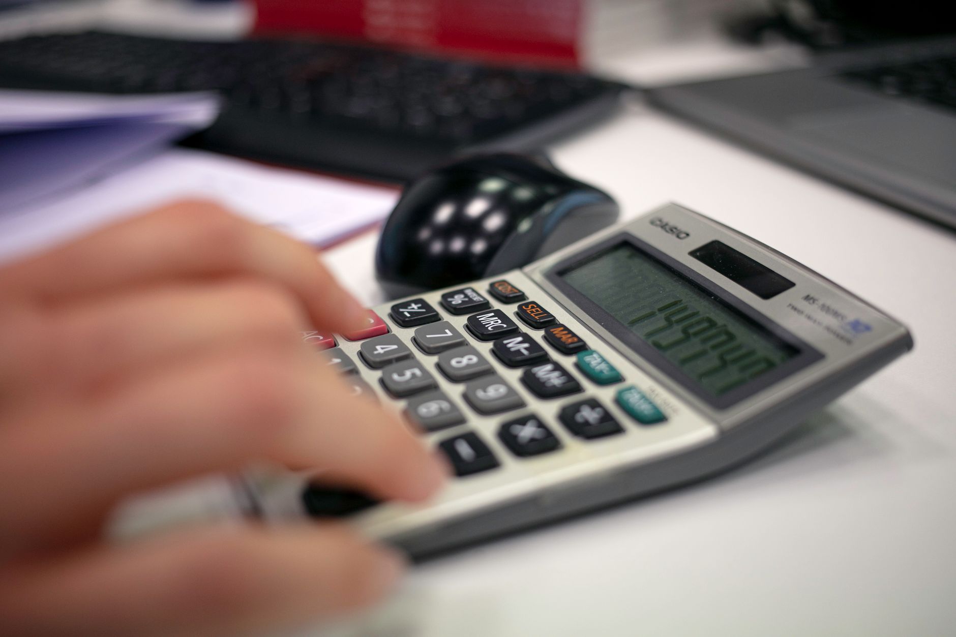 Gros plan sur une main utilisant une calculatrice posée sur un bureau de travail.